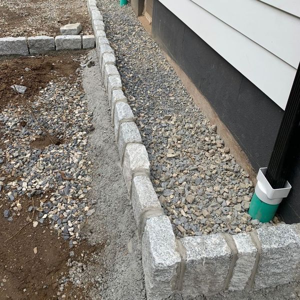 Granite border along a gravel-filled trench next to a white house with a black foundation.