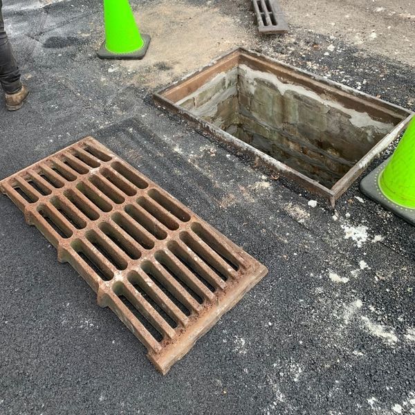 Open sewer manhole with a grate removed, asphalt, two traffic cones.