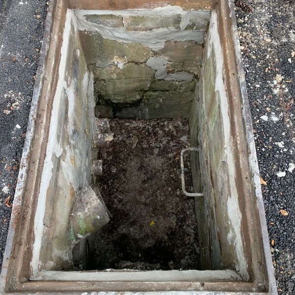 Open manhole with a ladder and debris inside.
