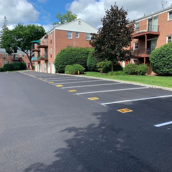 Asphalt parking lot with painted parking space lines. Apartment building in background. Sunny day.