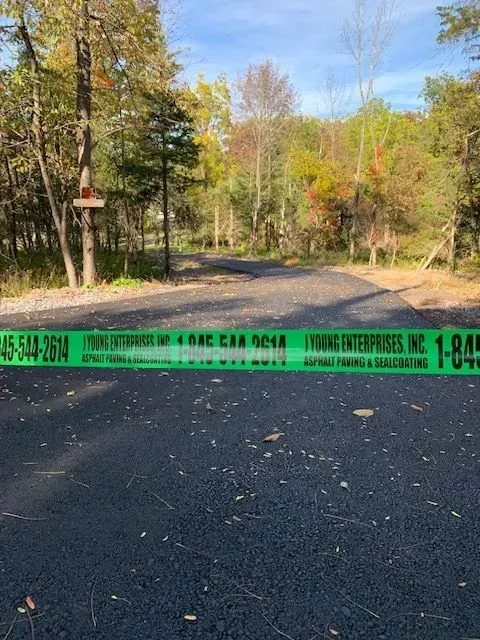 Newly paved road blocked by green caution tape with business contact information, trees in the background.