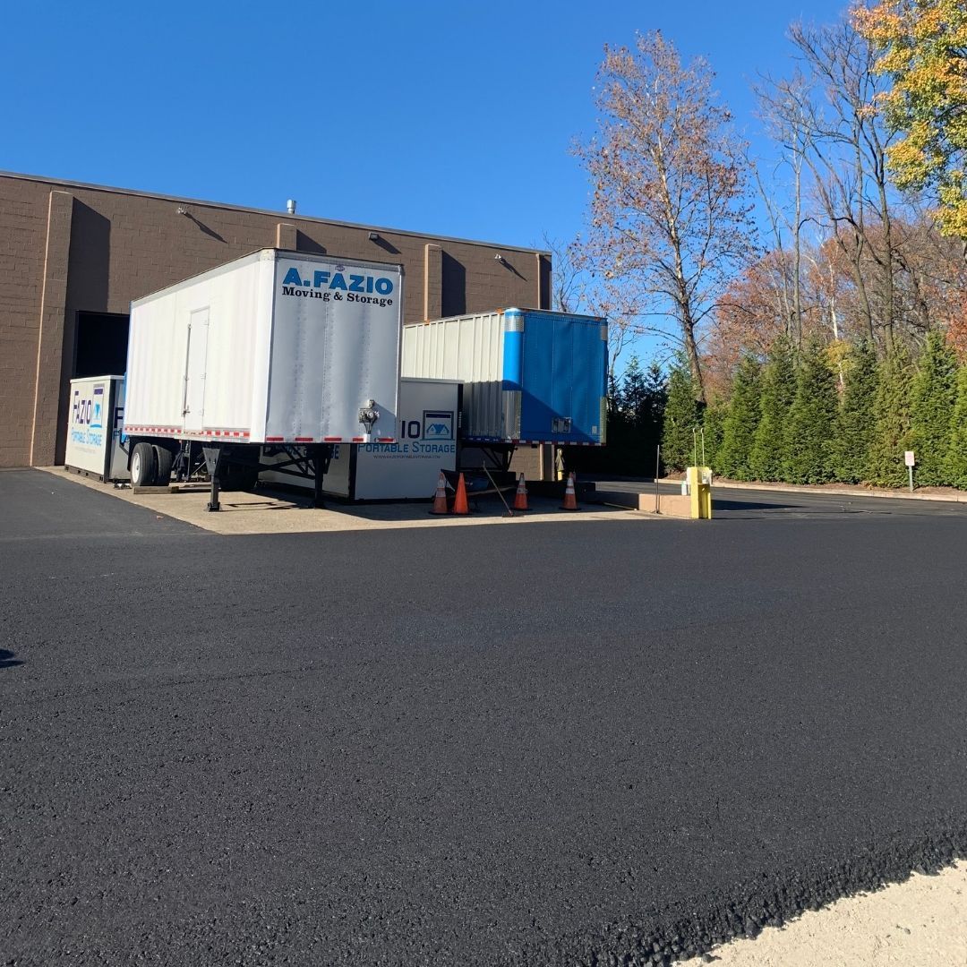 Blacktop parking area with tractor-trailers backed into a loading dock of a brick building on a sunny day.