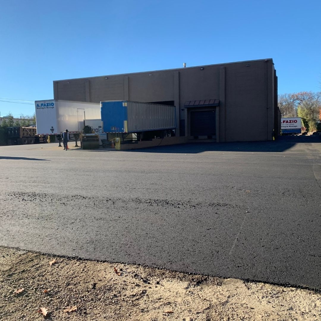 Loading dock with semi-trucks, in front of a large building, set in a paved parking lot.