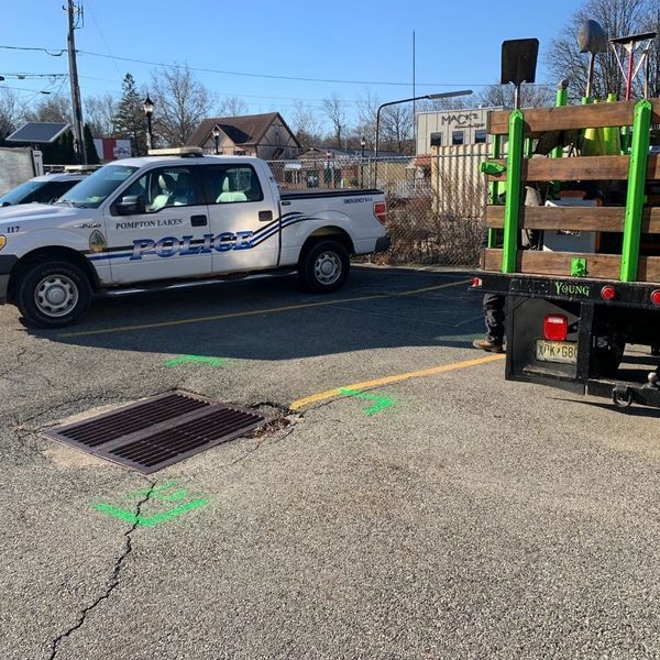 Police truck near sewer grate with green markings and a trailer. Outdoors in a parking lot.