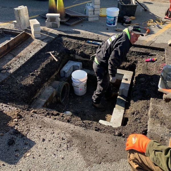 Man working in an excavated area with plumbing, tools, and construction materials.