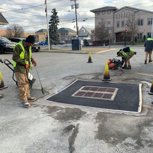 Construction workers paving around a manhole in an asphalt parking lot.