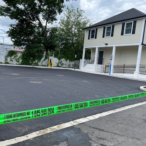 Newly paved asphalt parking lot next to a two-story building. Green caution tape across the foreground.