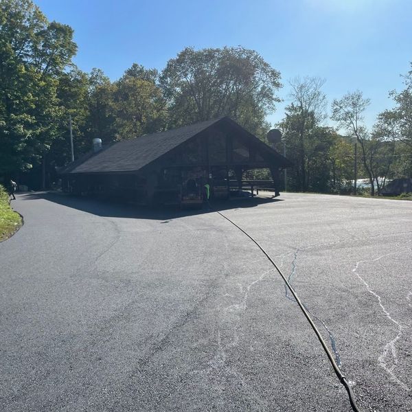 Asphalt parking lot with covered pavilion, trees and a lake in the background. Sunny day.