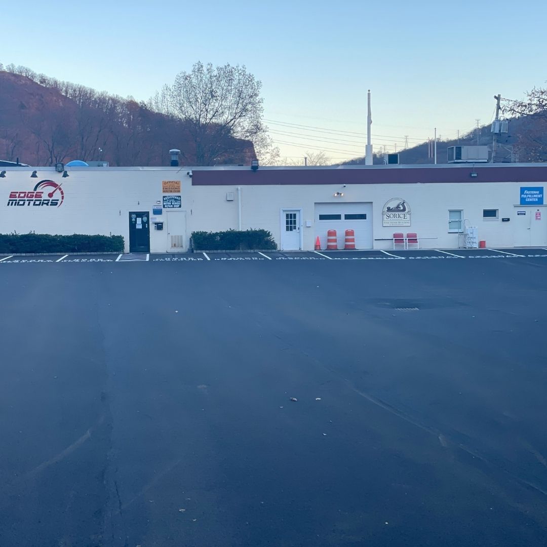 A one-story white commercial building with a black asphalt parking lot. A mountain is in the background.