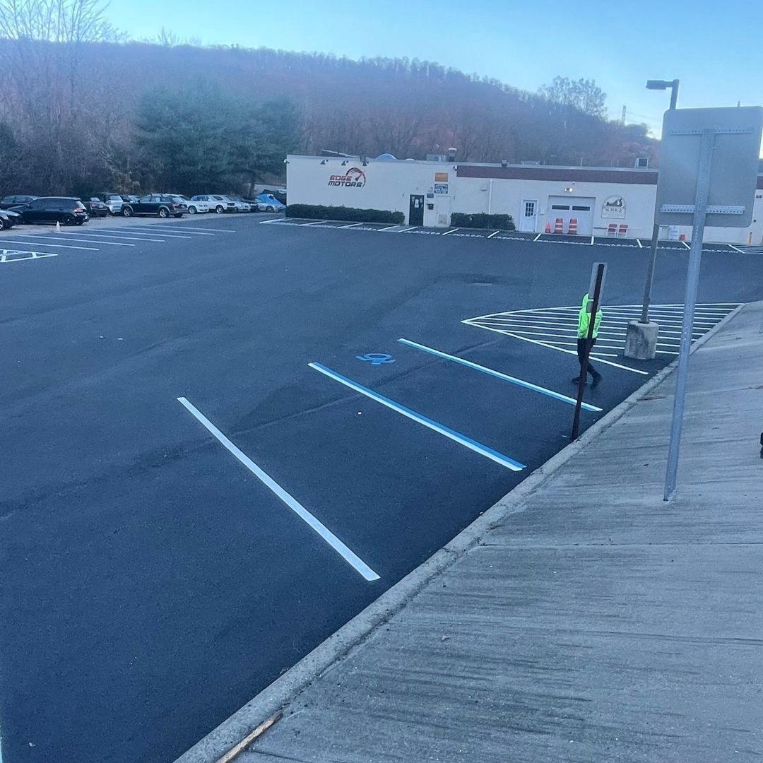 New asphalt parking lot with painted lines and a person in a vest; building in the background.