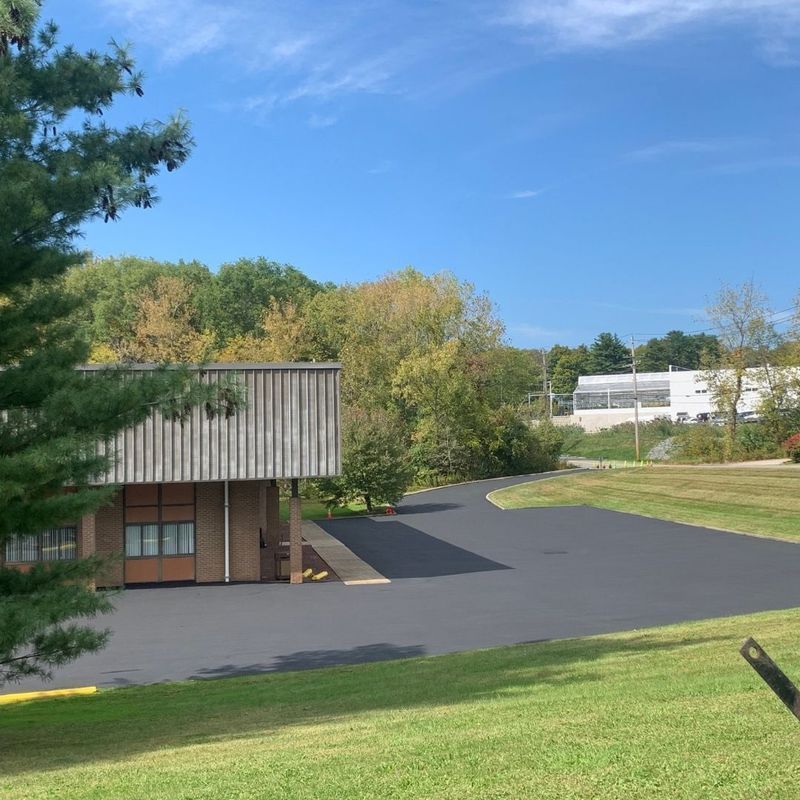 Building with a dark paved driveway and trees under a blue sky.