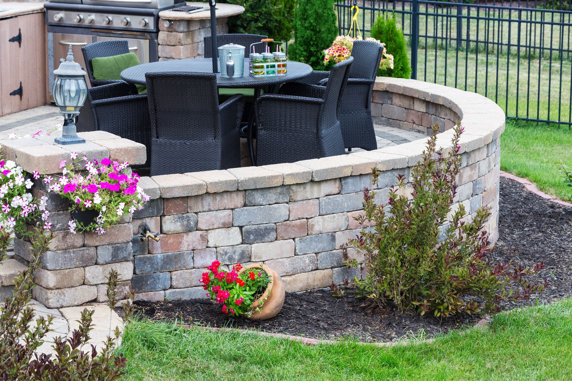 Outdoor patio with a circular table and chairs enclosed by a brick wall and landscaping.
