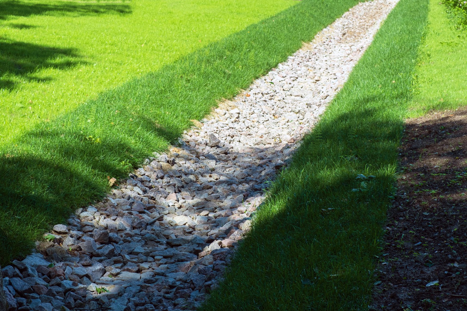 Stone-filled drainage channel between grassy lawns.