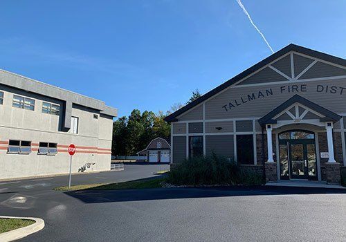 Exterior of Tallman Fire District building on a sunny day. Gray and brown buildings, paved lot, blue sky.