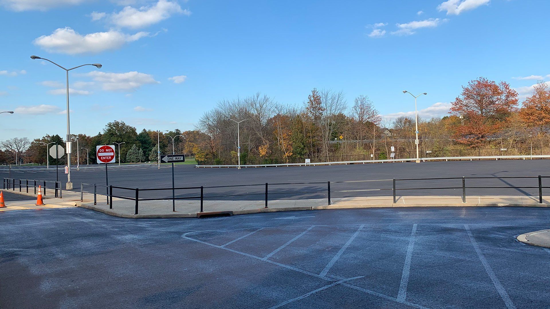 Empty parking lot with trees in the background, under a blue sky. A