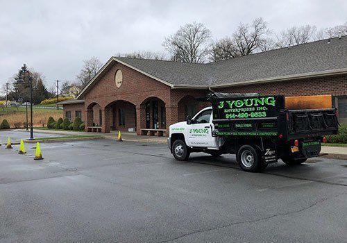 Dump truck in front of a brick building; green company logo, cones on the pavement.