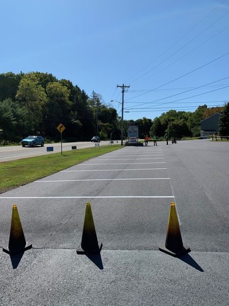 Empty parking lot with traffic cones, trees, and cars on the road under a blue sky.
