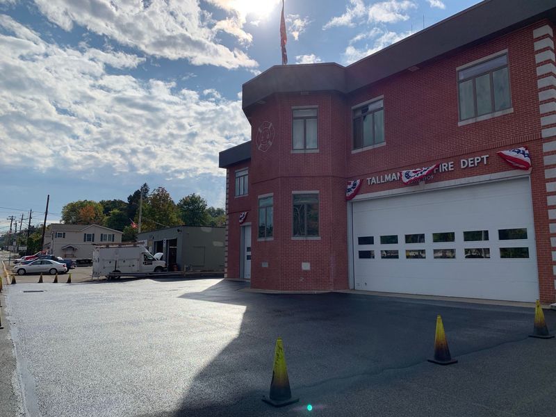 Exterior of a red brick fire station on a sunny day. Large garage door is closed; a flagpole on the roof.