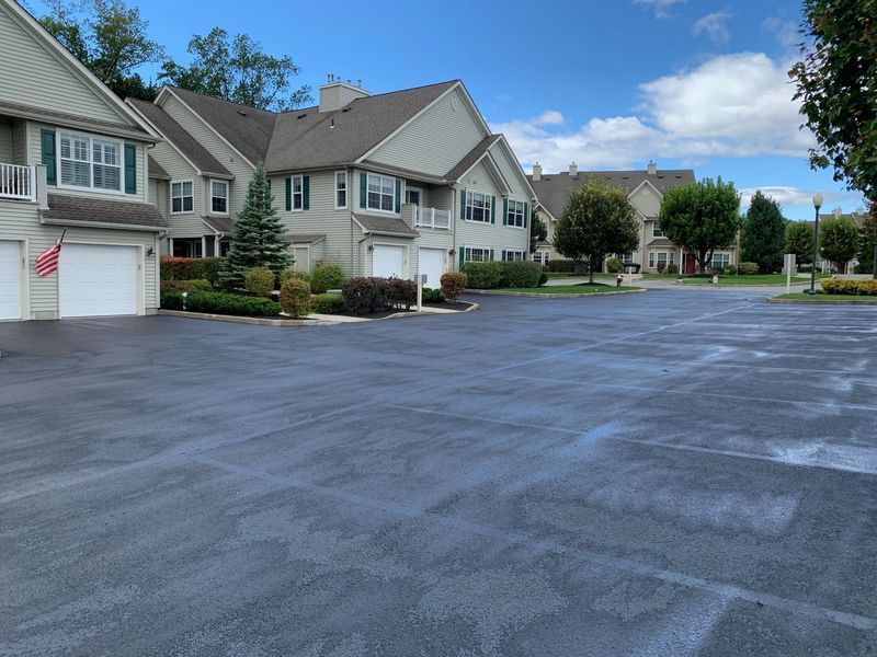 Asphalt parking lot in front of multi-unit residential buildings on a partly cloudy day.