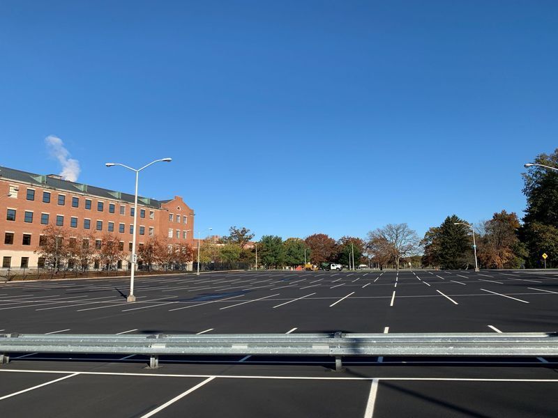 Empty asphalt parking lot with white lines, brick building in the background, blue sky.