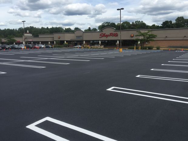 A freshly paved, empty parking lot with bright white painted lines, in front of a ShopRite grocery store under a cloudy sky.