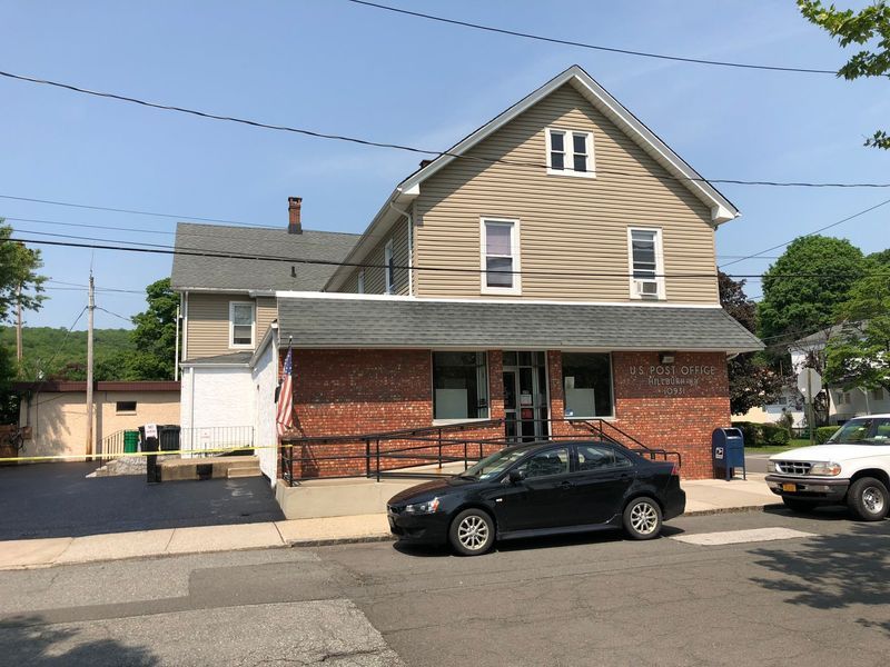 Two-story building with brick facade and accessible ramp. A black car and white truck are parked in front.