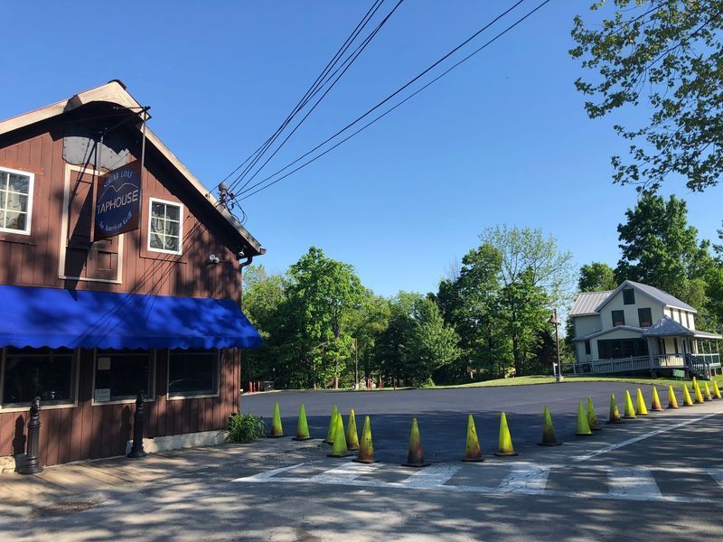 Brown building with blue awning; a house is across a paved lot, bright blue sky.