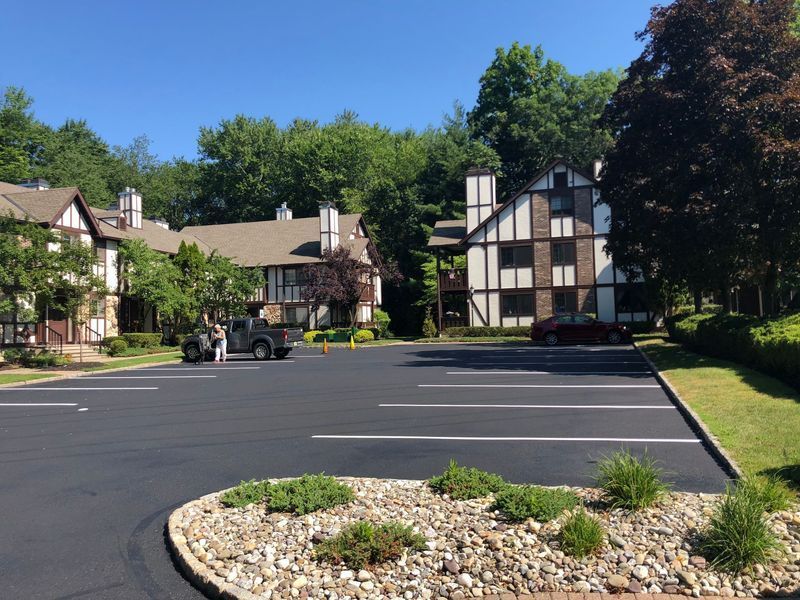 Parking lot in front of multi-story buildings with brown and white accents, surrounded by trees and a clear blue sky.