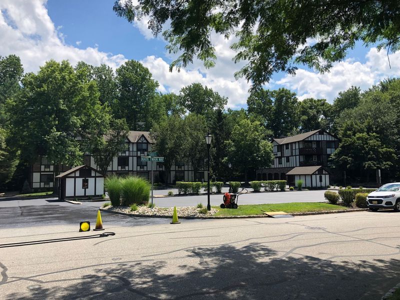 Buildings with Tudor-style architecture surrounded by trees, in a circular drive with a car and construction cones.