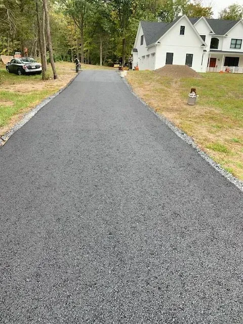 Newly paved asphalt driveway leading to a white house with landscaping.