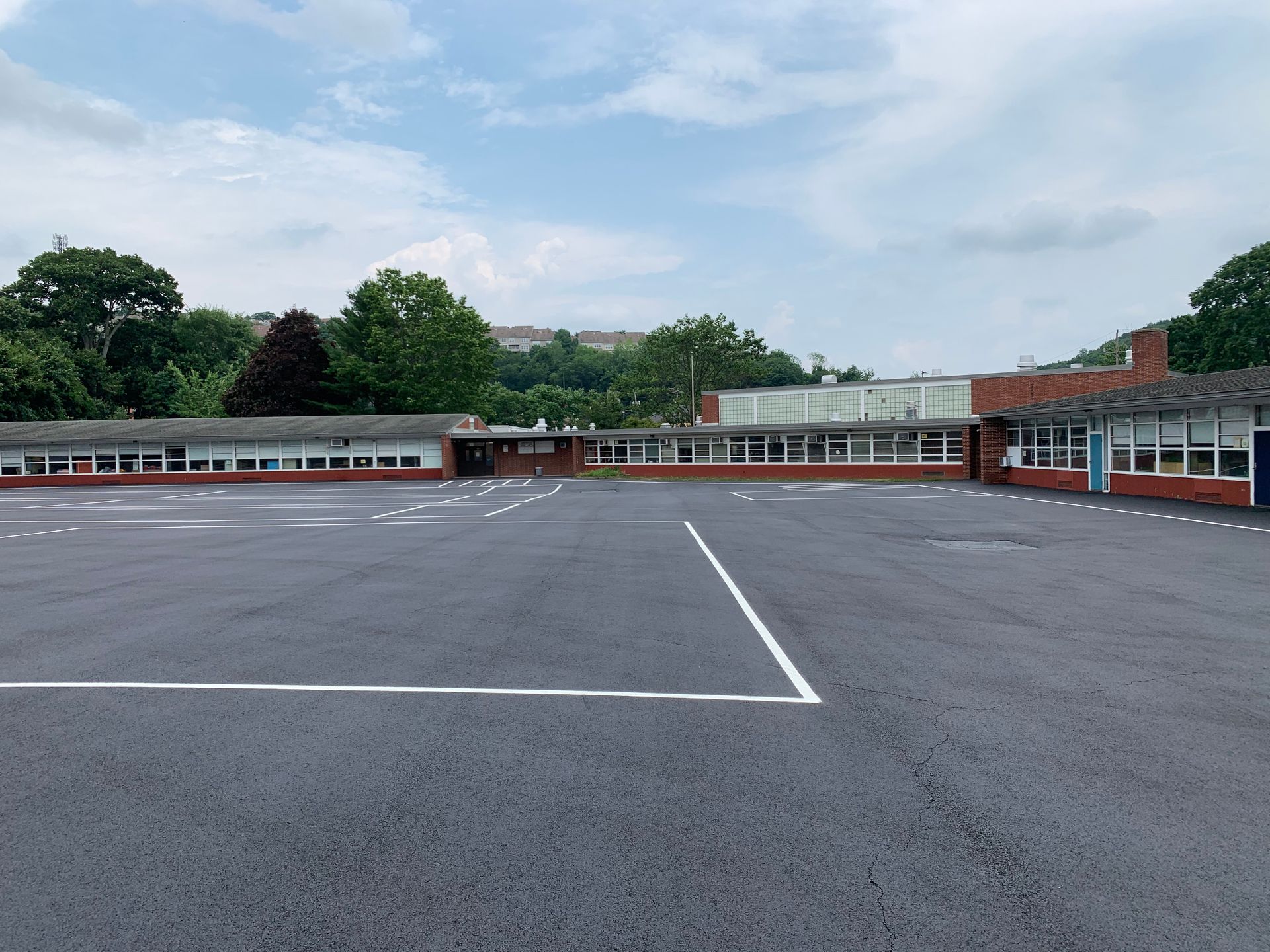 A large, empty school playground with white line markings on asphalt, bordered by a long, single-story red brick building.