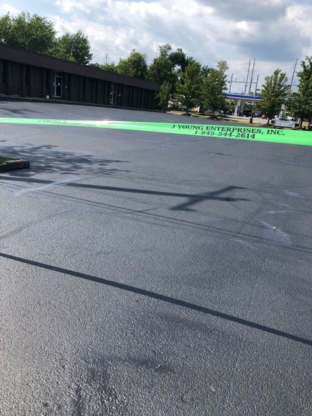 Freshly paved asphalt parking lot with a bright green stripe, sunlight casting long shadows.