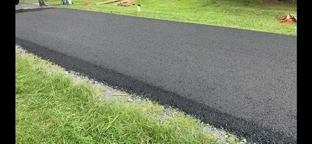 Newly paved asphalt pathway alongside green grass.