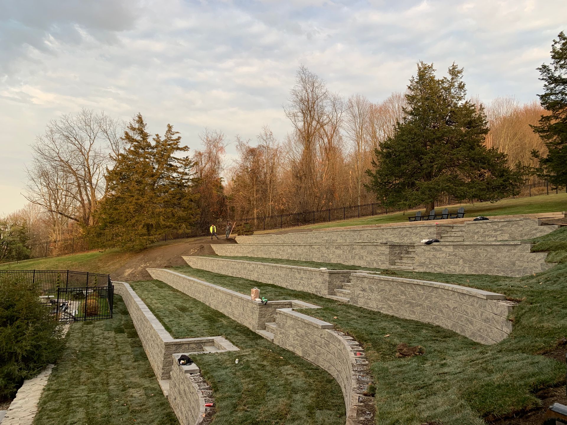 An outdoor stone amphitheater with tiered seating terraces built into a grassy hill, surrounded by trees at sunset.