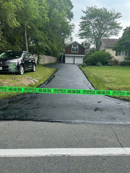 Black paved driveway with caution tape in front of a two-car garage. A black car sits to the left.