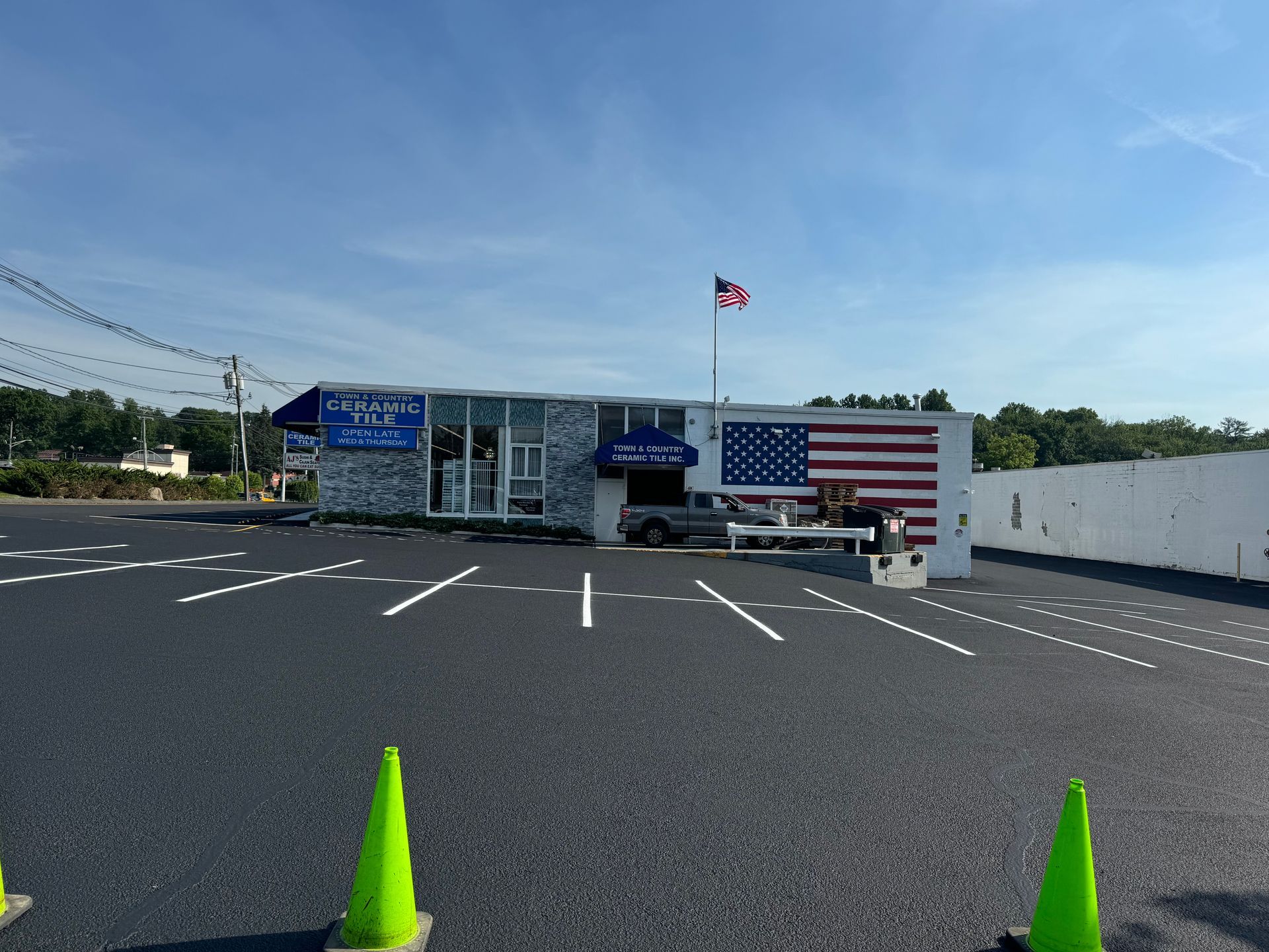 A commercial building with an American flag mural, a blue awning, and a freshly paved parking lot with two green cones.