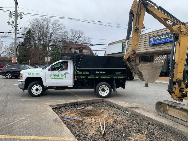 Excavator loading dirt into a J. Young dump truck at a construction site.