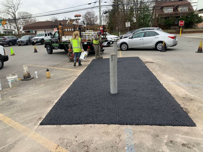 Asphalt repair in a parking area with workers, a utility truck, and parked cars.