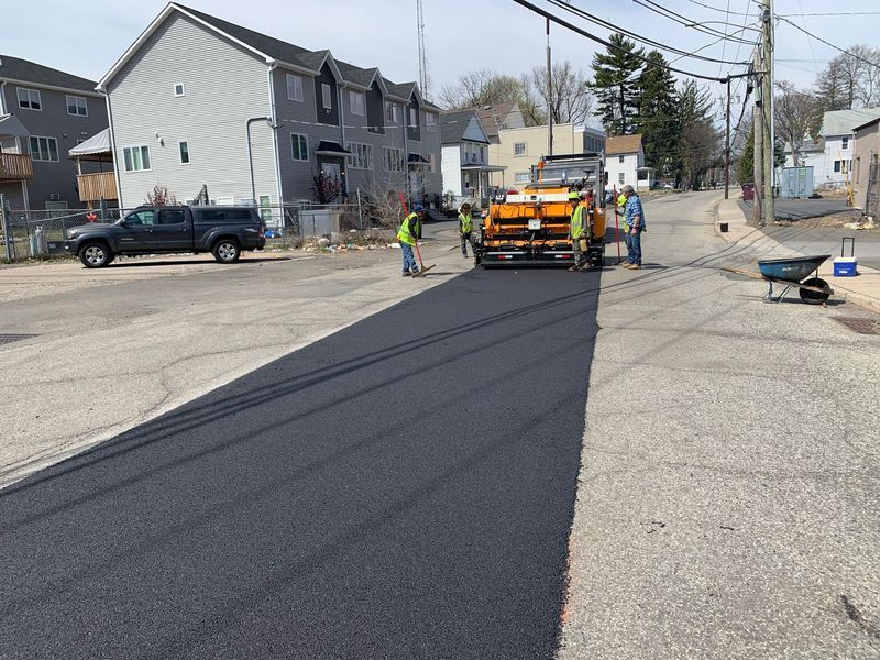 Road resurfacing: asphalt paving crew with machinery and fresh black asphalt on a street.