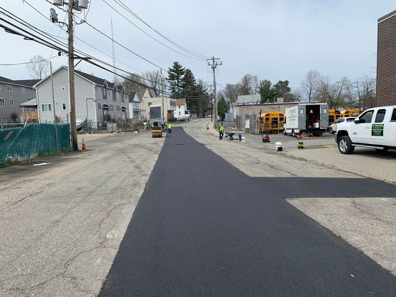 Freshly paved street with construction workers and equipment; residential neighborhood.