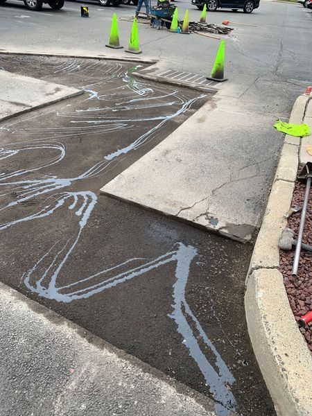 Asphalt patch with gray sealant. Concrete sections, traffic cones, and tools are present.