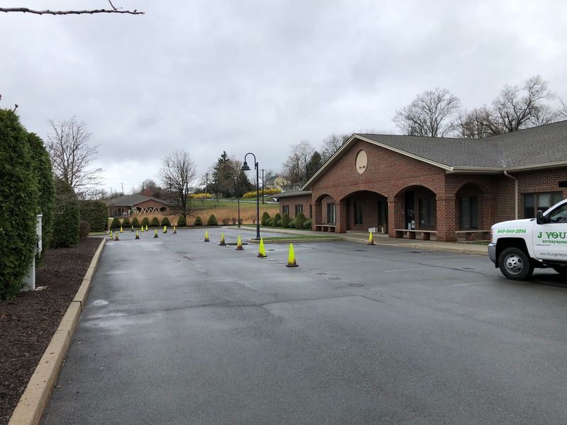 A brick building with a parking lot cordoned off by traffic cones. A green truck is parked on the right. Overcast skies.