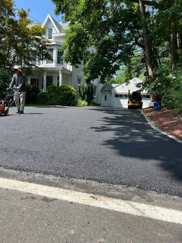 Man paving a driveway with a machine in front of a white house with a two-car garage.
