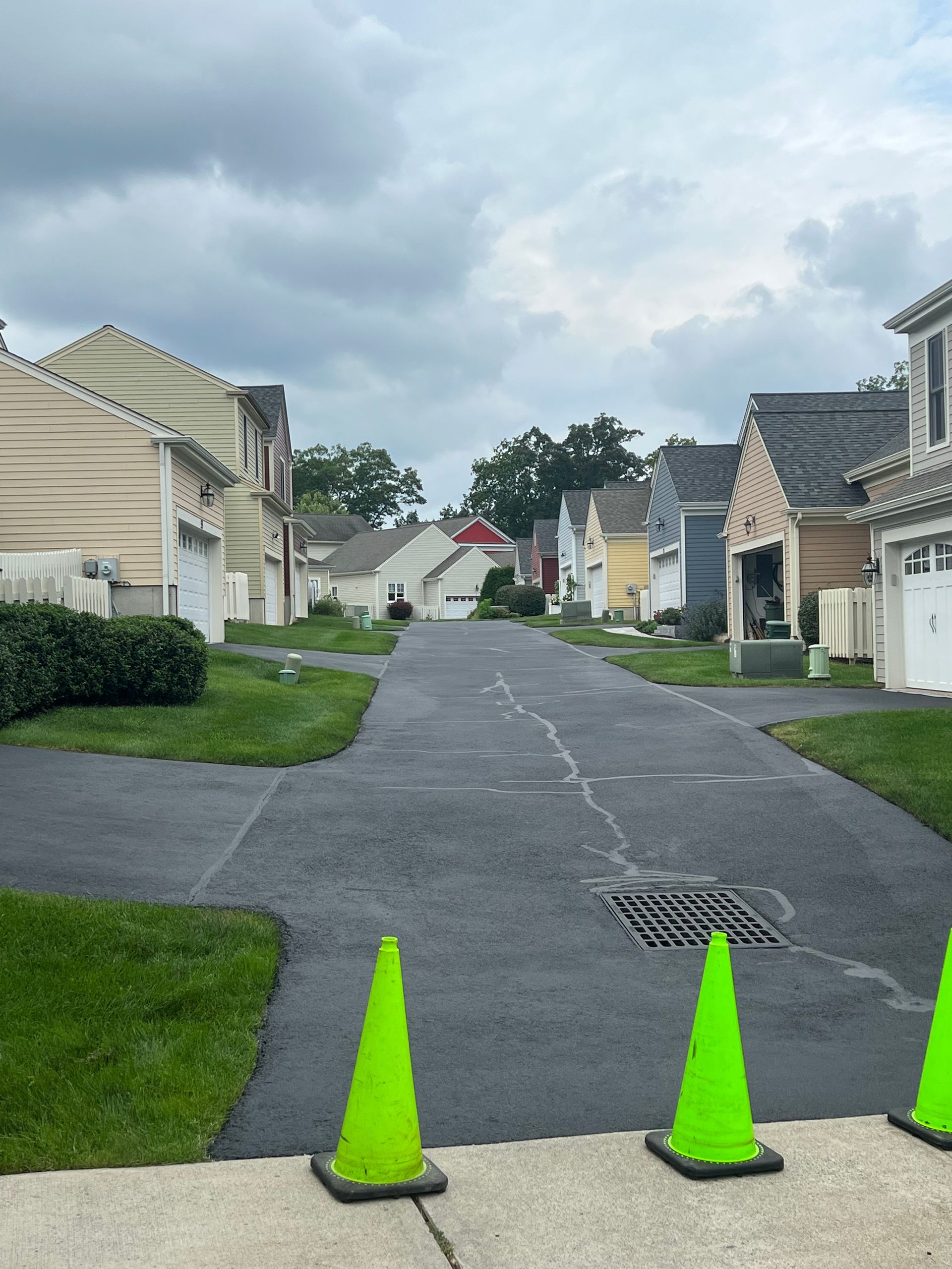 A paved alleyway between suburban houses, with three bright lime-green traffic cones in the foreground.