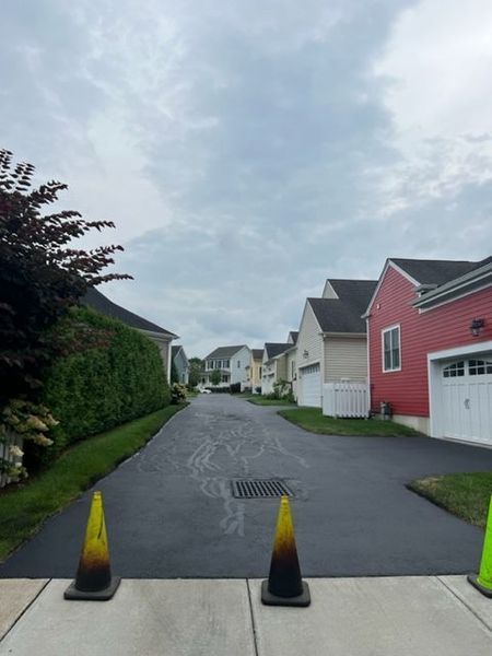 Asphalt driveway with cones, houses and cloudy sky.