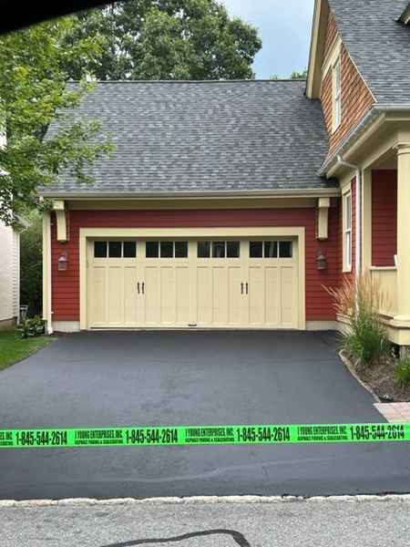 Red-sided house with beige garage door, dark driveway. Green caution tape across the bottom.