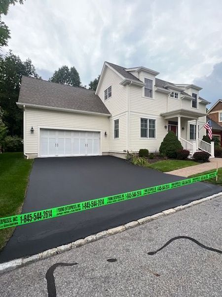 House with newly paved black driveway, green tape across it, cloudy sky.