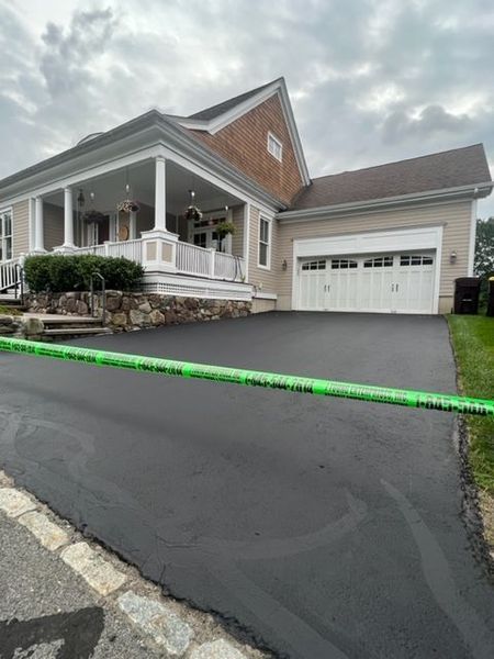House with a freshly paved asphalt driveway, front porch with columns, and a garage under a cloudy sky.