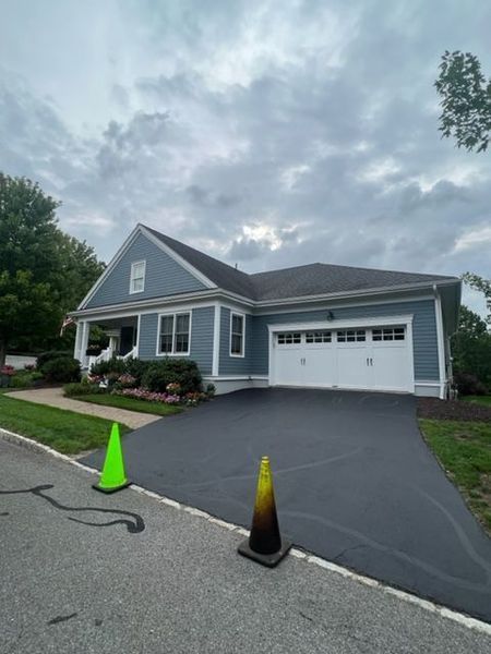 Blue house with white trim, a black driveway, and two traffic cones in front.