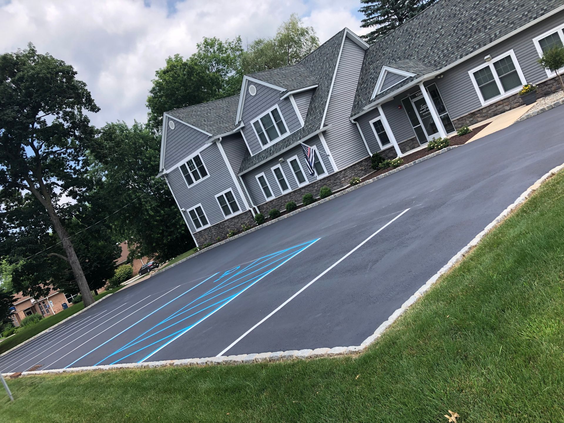 A gray building with an asphalt parking lot featuring blue painted lines for handicap-accessible parking spaces.